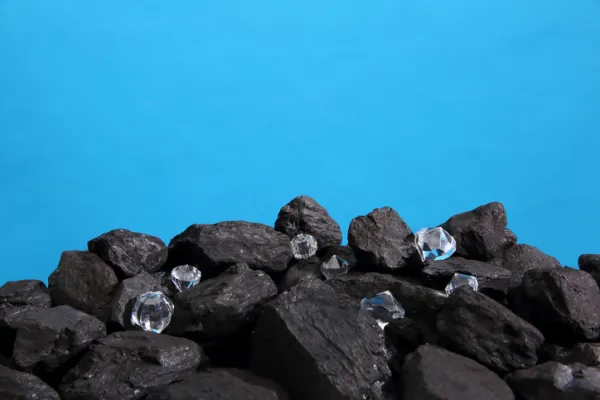 Black coal is strewn on a prism on a blue background and among it there are polished diamonds.