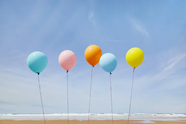 Five colorful balloons in a row at beach against blue sky