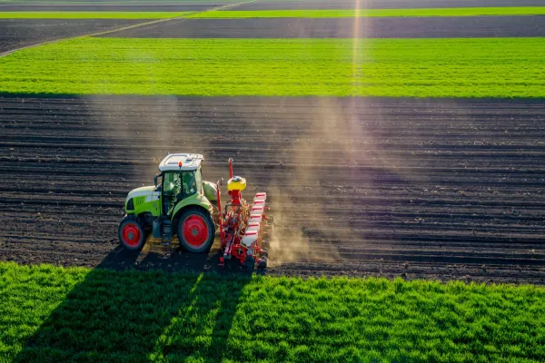 Aerial view of tractor as dragging a sowing machine over agricultural field, farmland