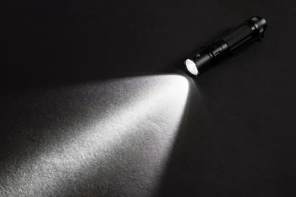 Flashlight and a beam of light in darkness. A modern led lamp with bright projection on dark wood table.