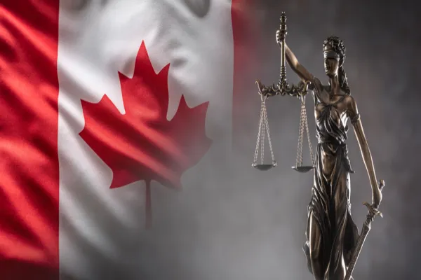 Justice is blind statue symbolizing law with scales and sword in hands and a Canadian  flag in the background.