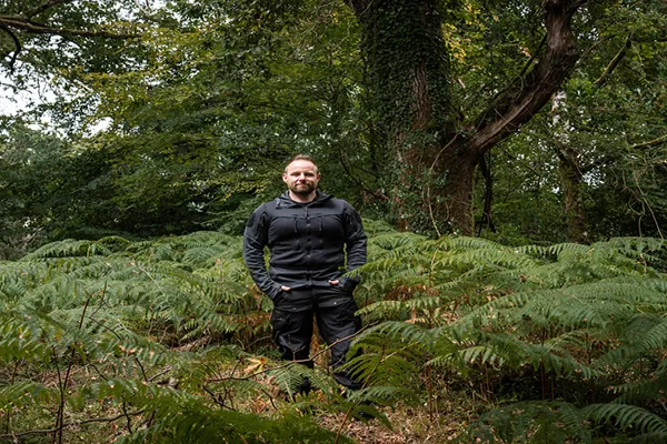 Man standing among green ferns in a forest with tall trees overhead