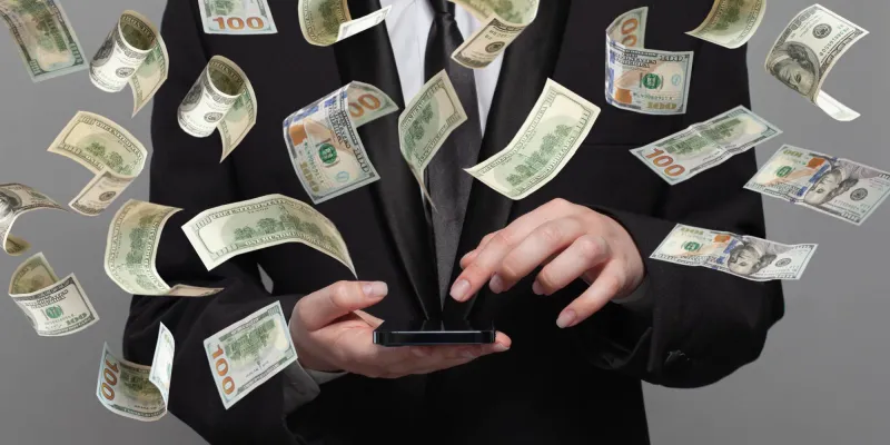 Person in suit works on mobile phone under money rain on grey background