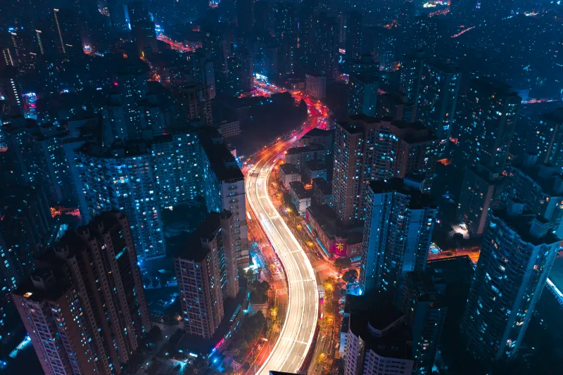 A cityscape at night with illuminated skyscrapers and a brightly lit highway winding through.
