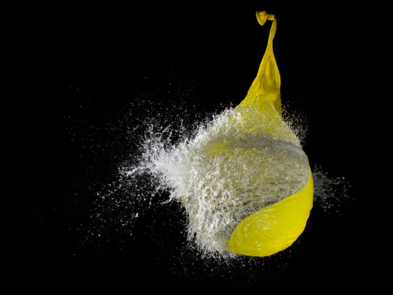 Yellow waterballoon bursting against black background, close up