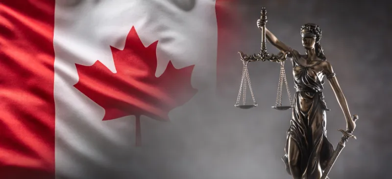 Justice is blind statue symbolizing law with scales and sword in hands and a Canadian  flag in the background.