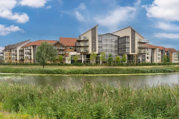 Luxury residential building with red roofs, near a water body and green grass.